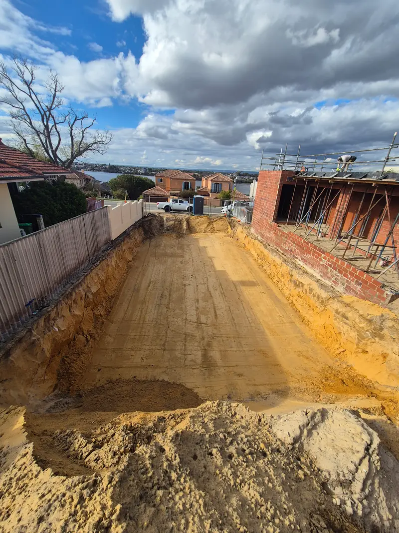 Residential basement excavation beside a brick boundary wall, overlooking the suburbs