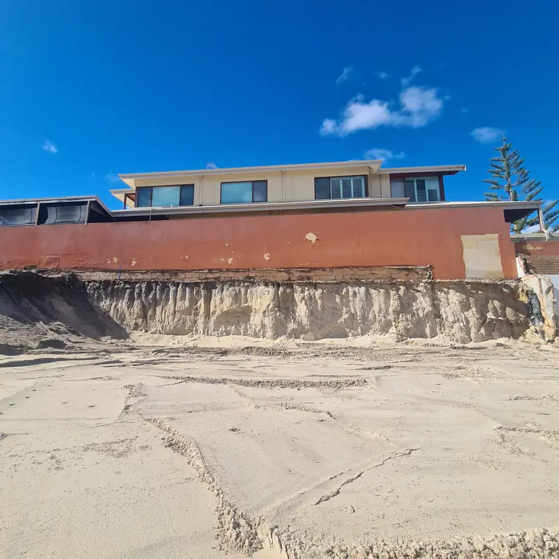 Wide excavation with a stabilised soil face running beneath a neighbouring two-storey building
