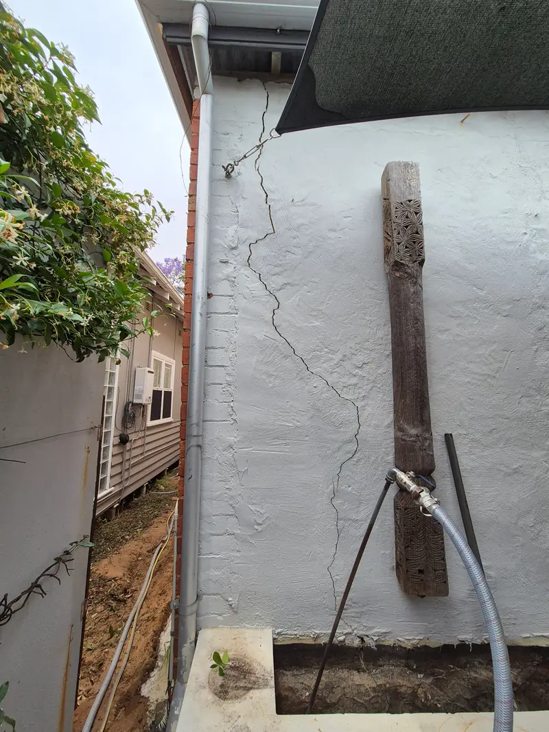 Grout injection hose and lance set up alongside a cracked rendered wall
